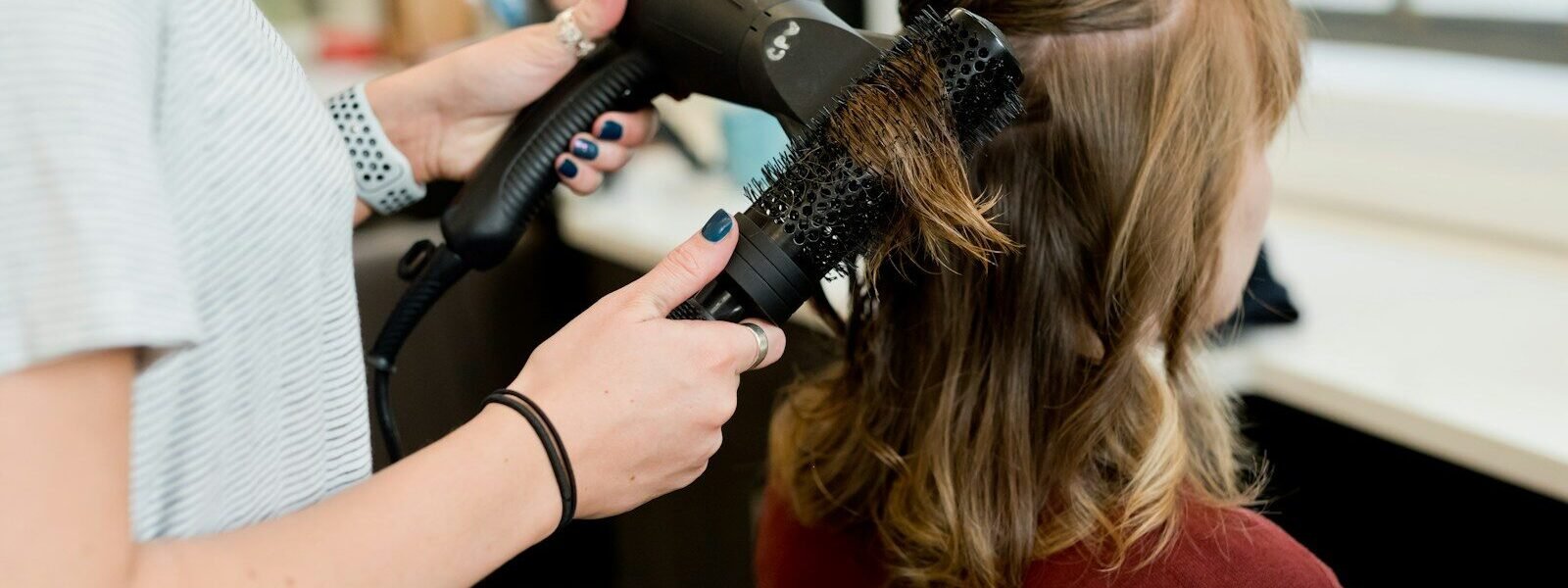 A hairstylist using a blow dryer and round brush on a client's hair
